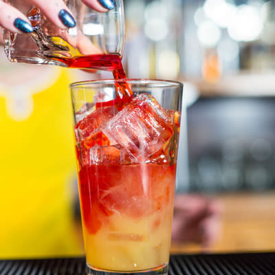 pouring a red colored liquor into a pint glass with ice and orange juice