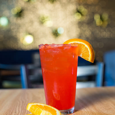 a bright orange-red cocktail in a pint glass with an orange garnish