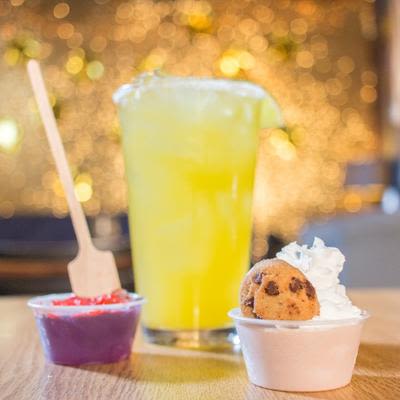 A glass of yellow cocktail and a small cup with a cookie and whipped cream