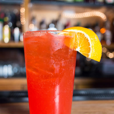 a bright orange-red cocktail in a pint glass with an orange garnish