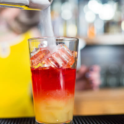 pouring sugar into a pint glass filled with ice, and layered orange juice and Campari, a bright red liquor