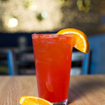 a bright orange-red cocktail in a pint glass with an orange garnish