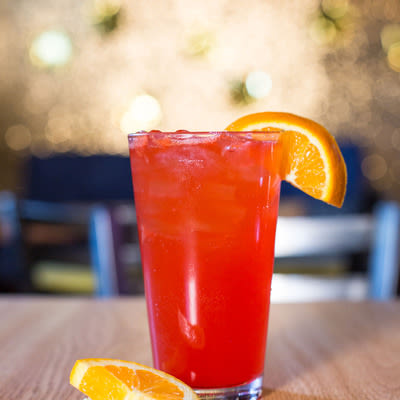 a bright orange-red cocktail in a pint glass with an orange garnish
