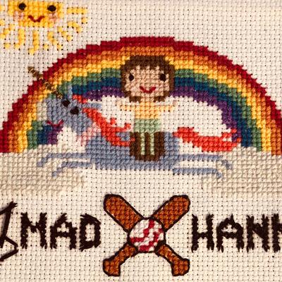 Cross stitch of a child on a unicorn under a rainbow including Mad Hanna Logo