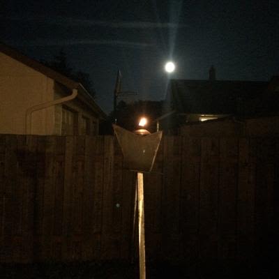 a lit tiki torch in the shape of the Mad Hanna logo of a top hat at night under the moon