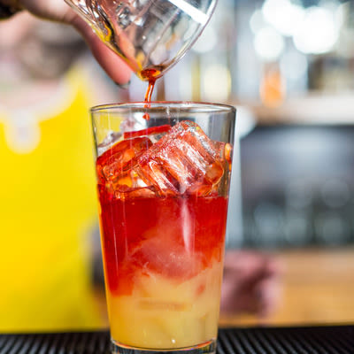 pouring a red colored liquor into a pint glass with ice and orange juice