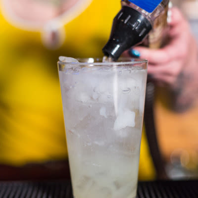 Adding a splash of soda to a cocktail in a pint glass