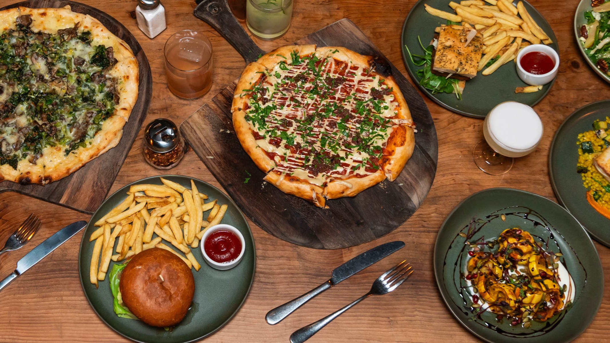Organic Berkeley food on table, including two pizzas, a burger and side dishes at Gather restaurant