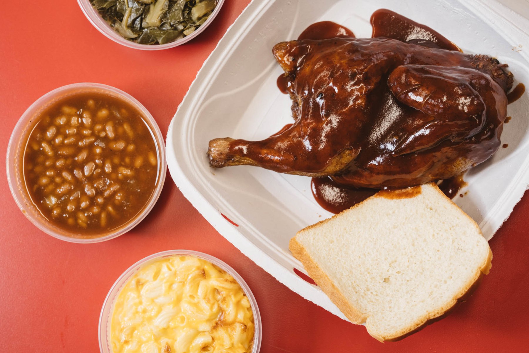 A BBQ chicken meal with sides of mac and cheese, baked beans, and collard greens.