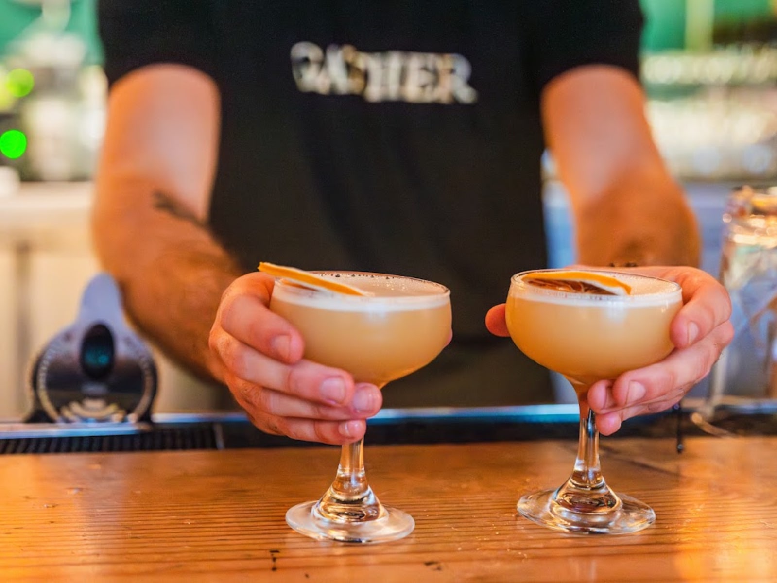 Close-up of bartender serving two Flor de Fuego grapefruit-shaded cocktails at bar of Gather in Berkeley restaurant